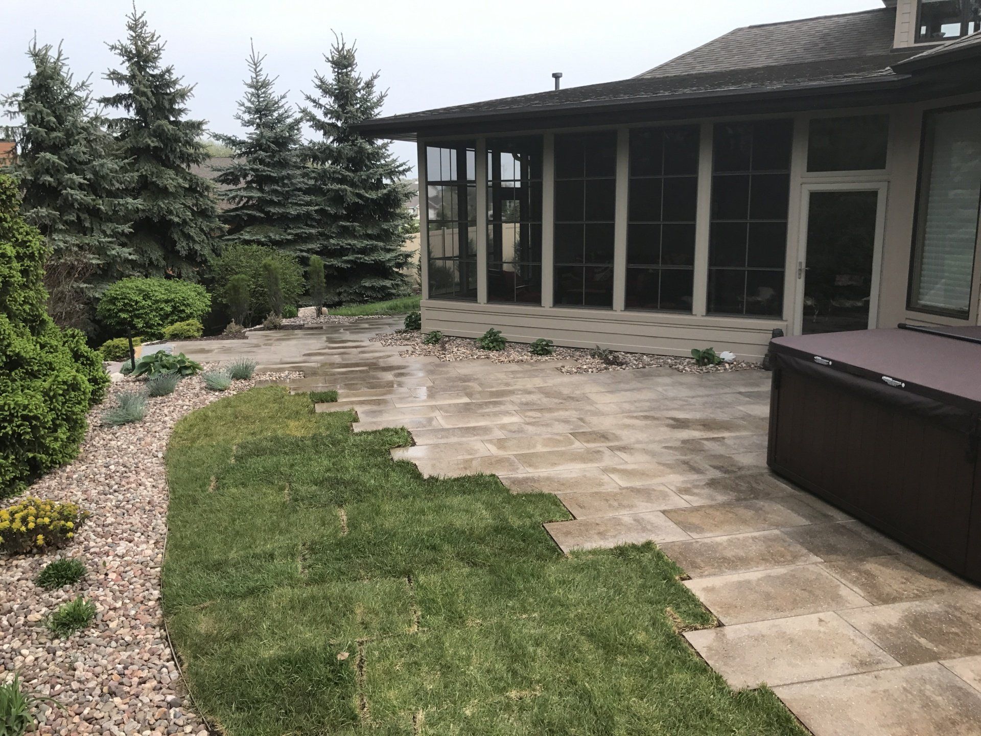 Backyard patio with stone pavers and partial sod install, adjacent to a screened-in porch and hot tub.