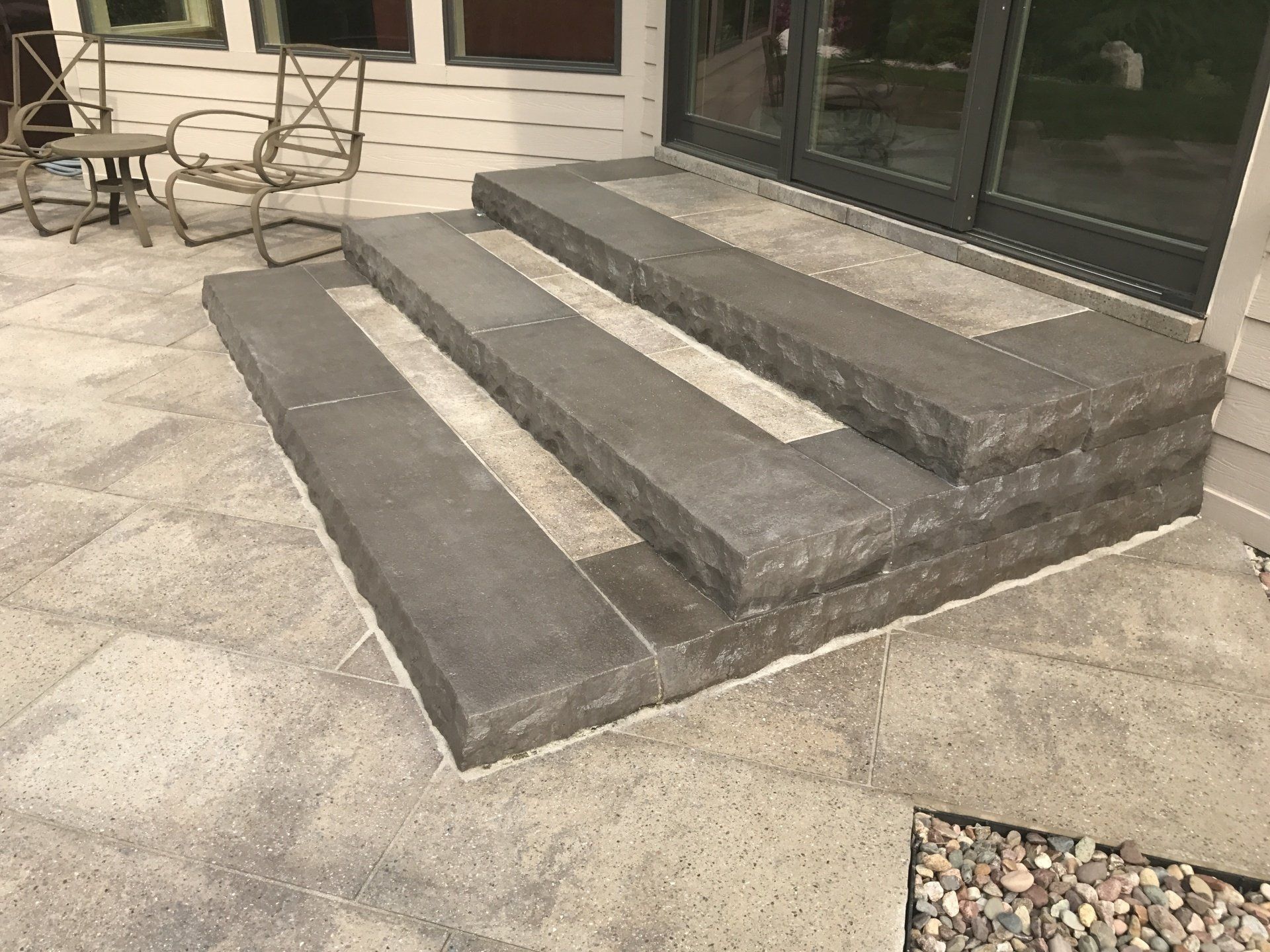 Stone steps leading up to glass sliding doors on a gray patio.