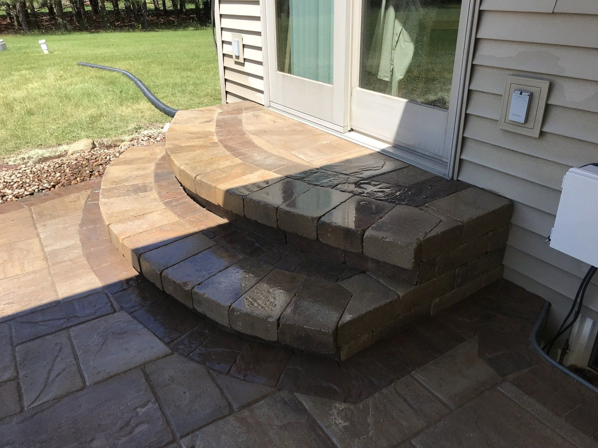 Stone steps leading up to glass doors on a house with a surrounding paved patio.