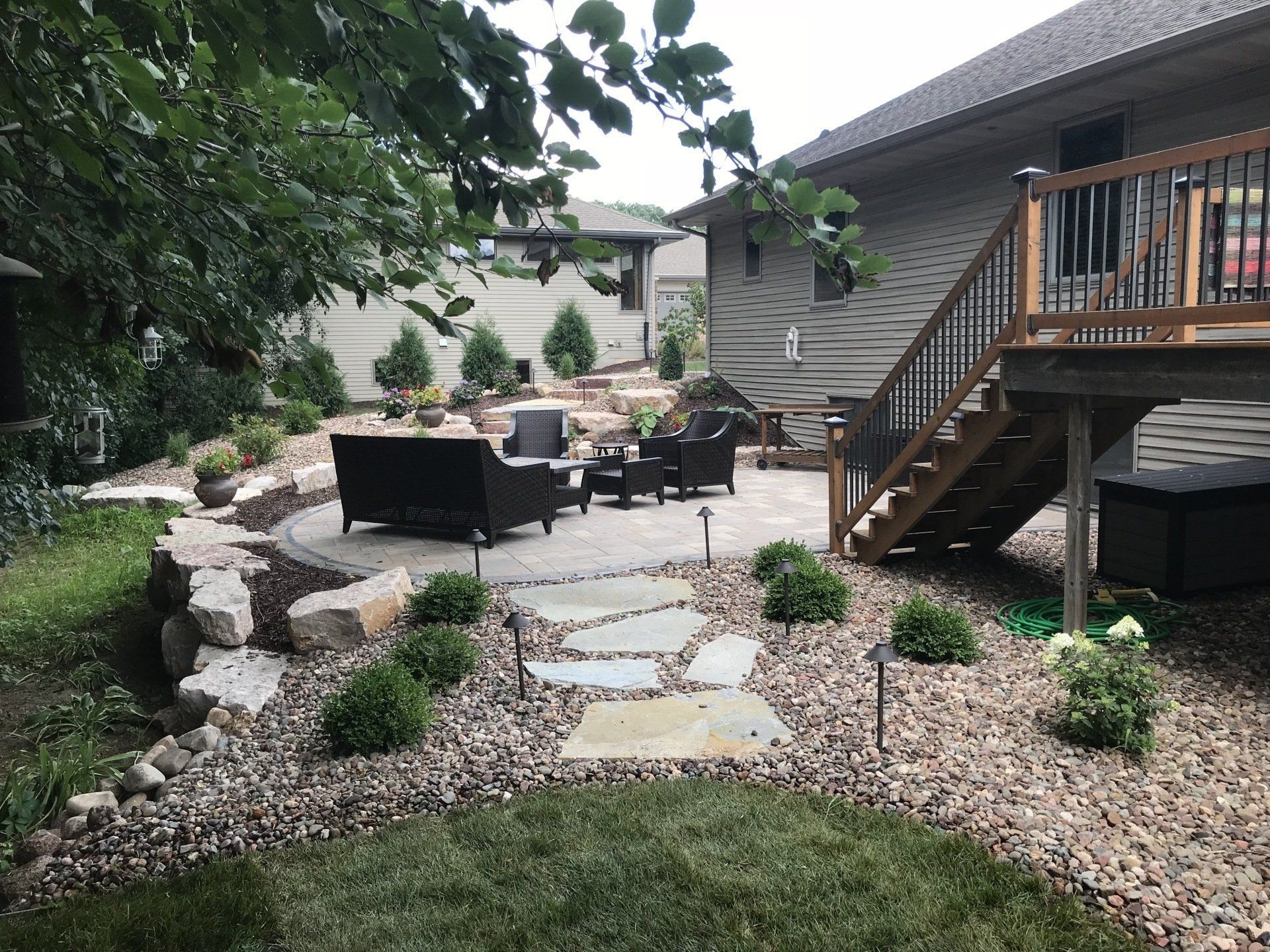 Backyard patio with seating, fire pit, stone walkway, and landscaping. A home is in the background.