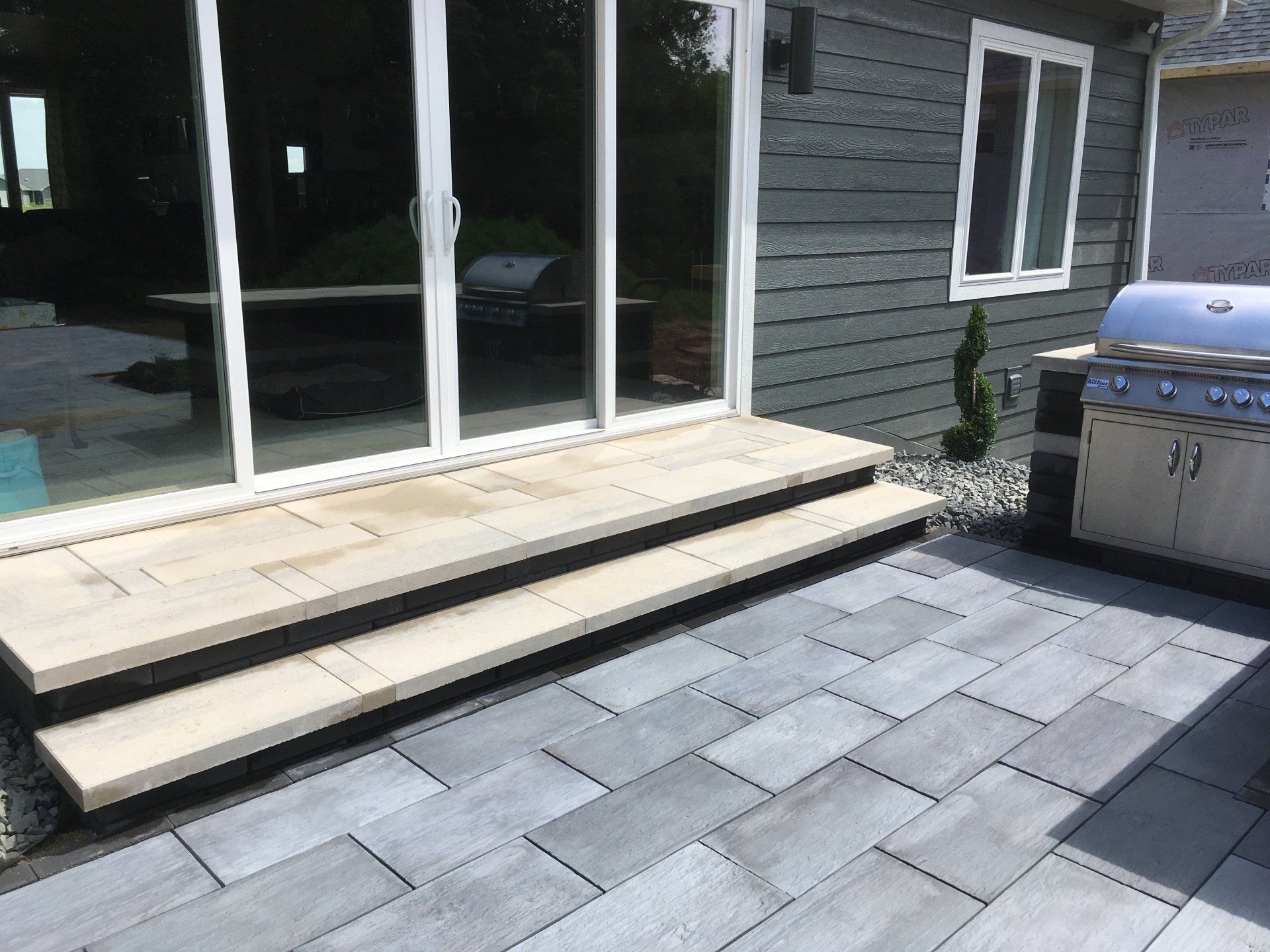 Patio with stone pavers, steps leading to sliding glass doors, and a barbecue grill.