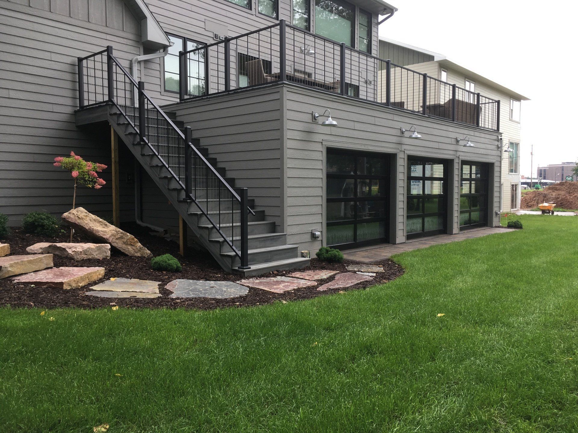 Grey house with deck, stairs, glass doors, and manicured lawn. Black railings and trim.