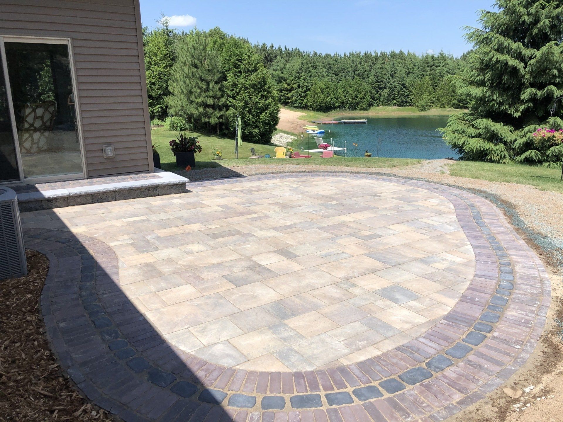 A brick patio with a circular border near a lake and trees.