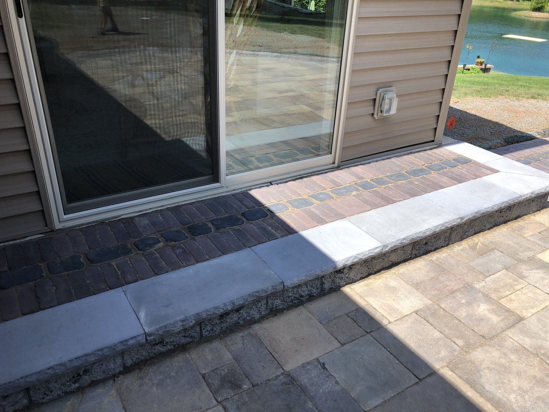 Brick patio with stone steps leading to a sliding glass door. A small pond is visible in the background.