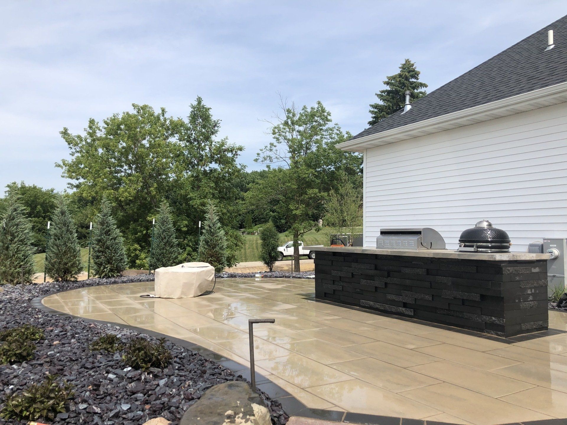 Outdoor patio with barbecue area, stone work, trees, and cloudy sky.