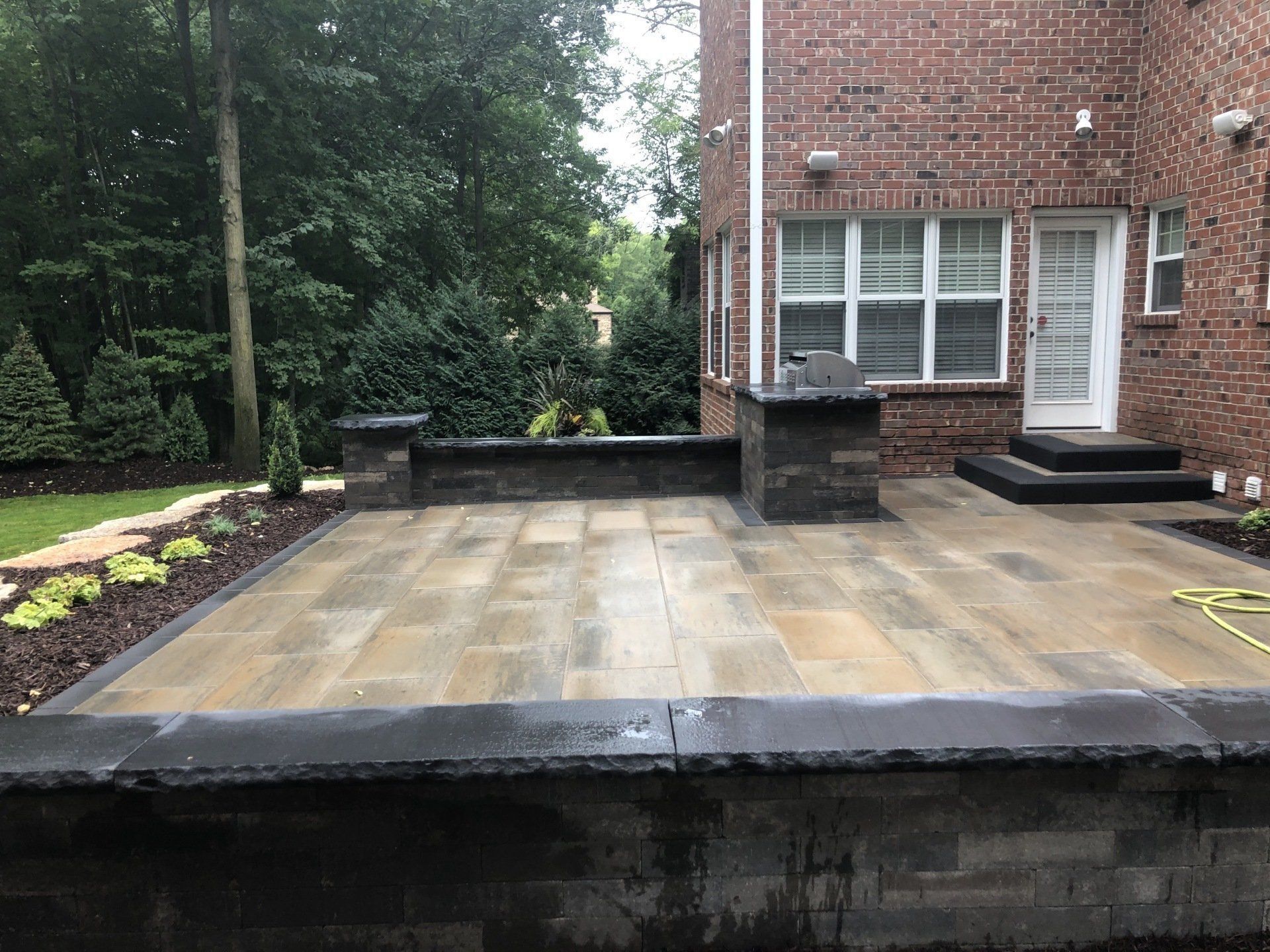 Stone patio with brick house, small retaining walls, and surrounding greenery.