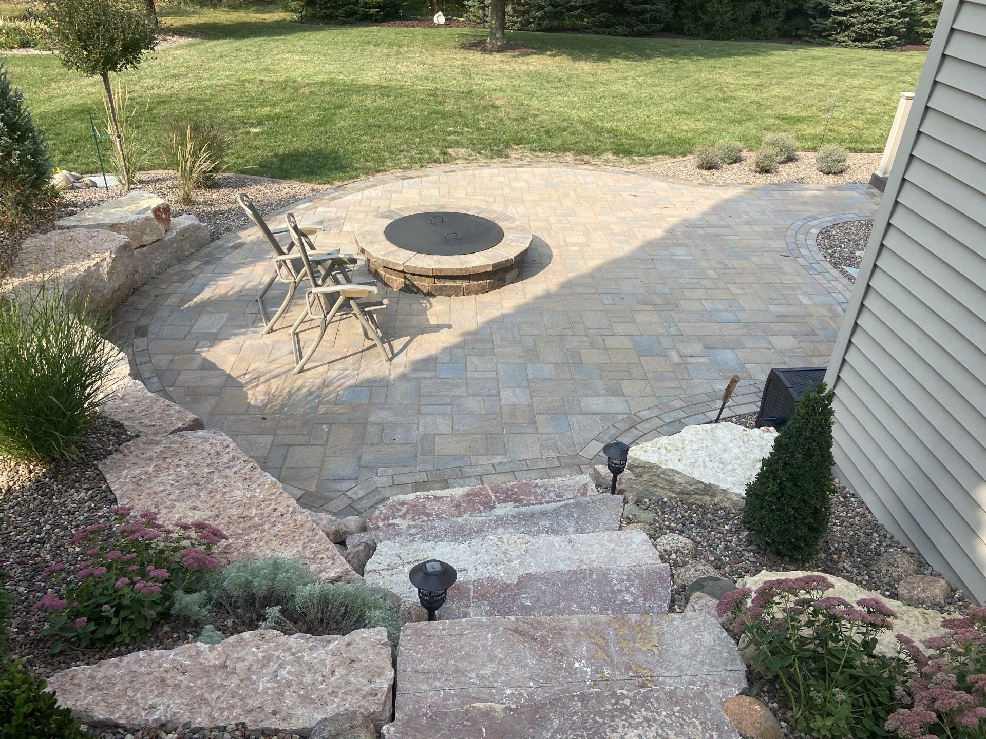 Stone patio with fire pit, seating, and stairs leading up from a terraced garden.