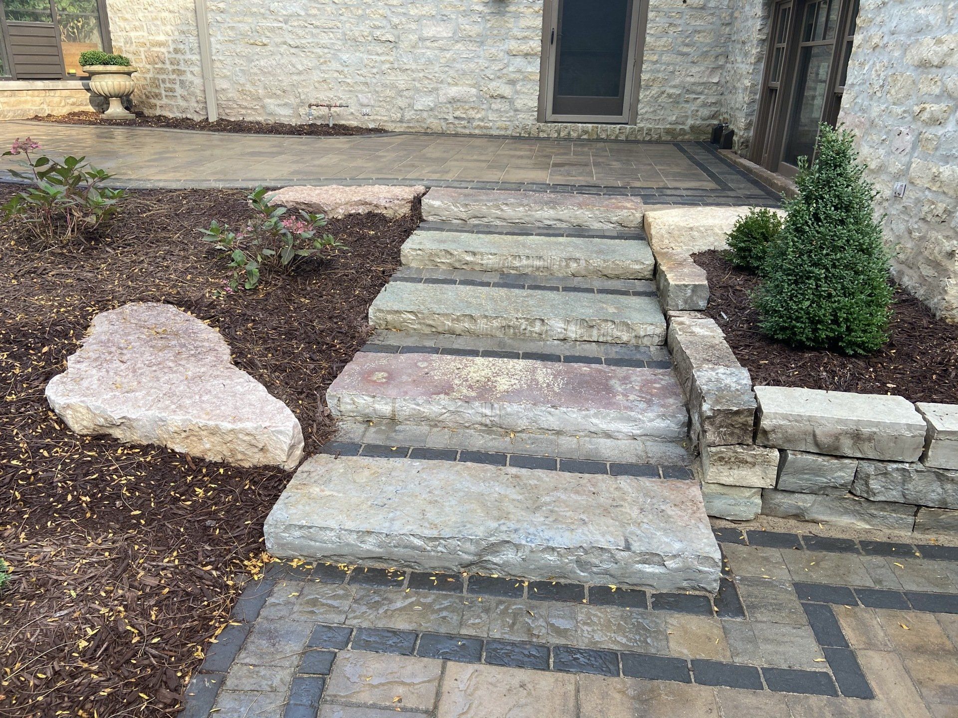 Stone steps leading up to a patio, surrounded by landscaping and a stone wall.