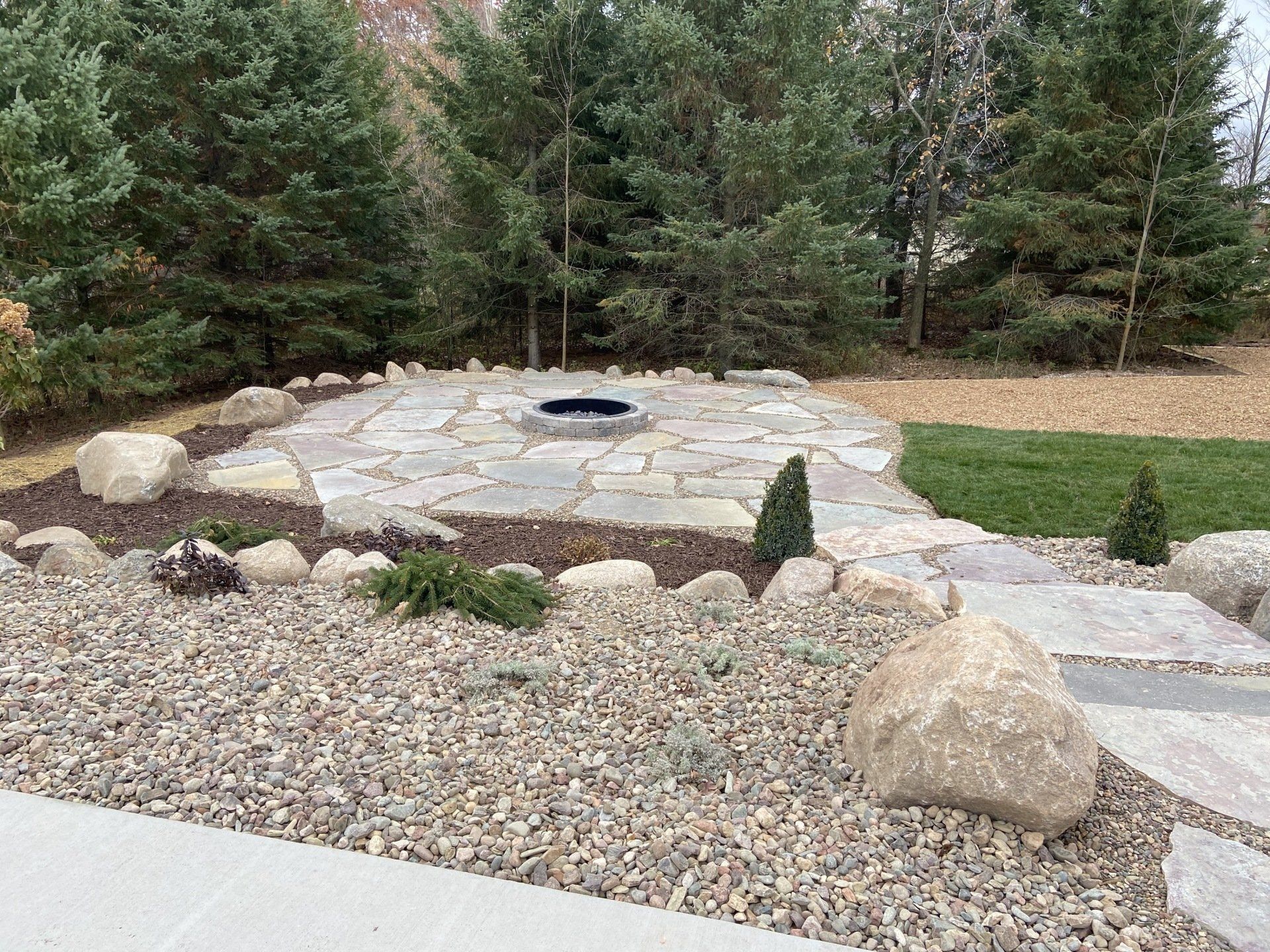 Fire pit patio with natural stone and gravel landscaping, with trees in the background.