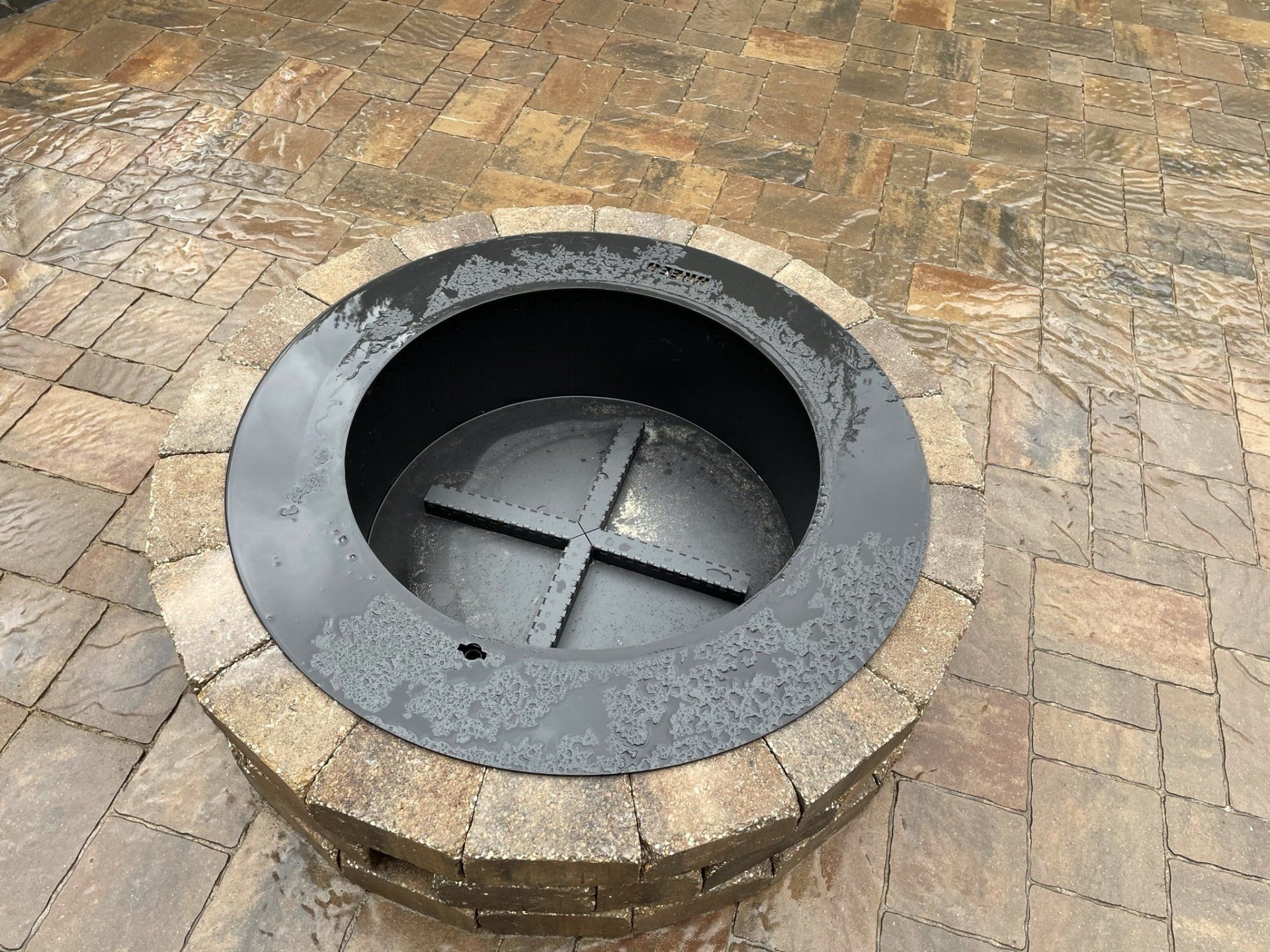 Fire pit with a stone border on a wet brick patio.