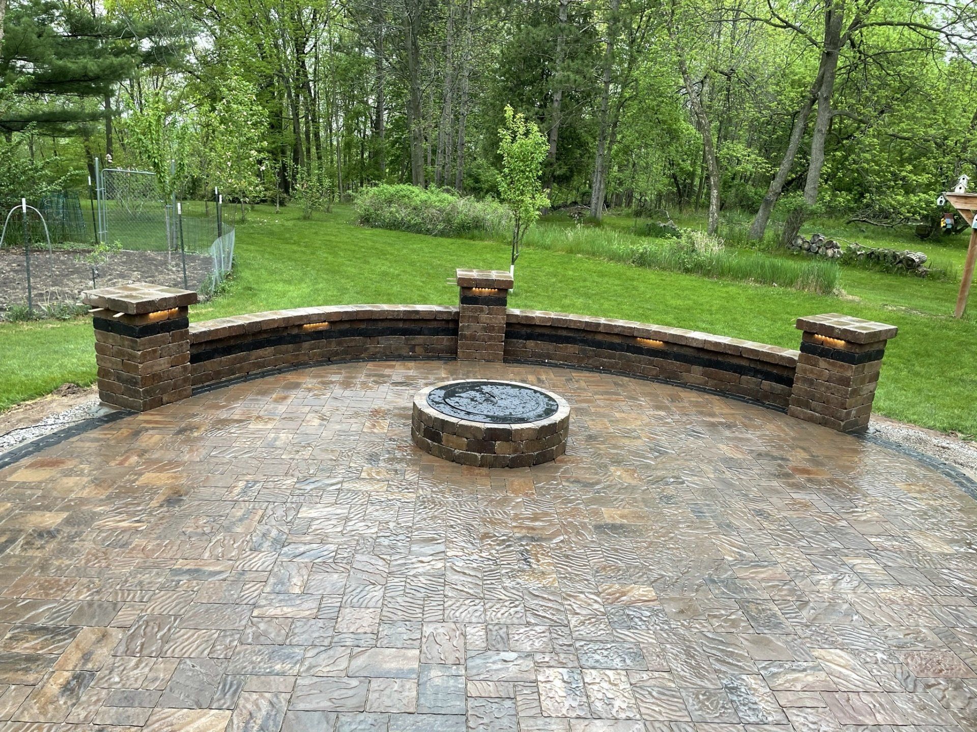 Stone patio with curved wall, fire pit, and surrounding trees.