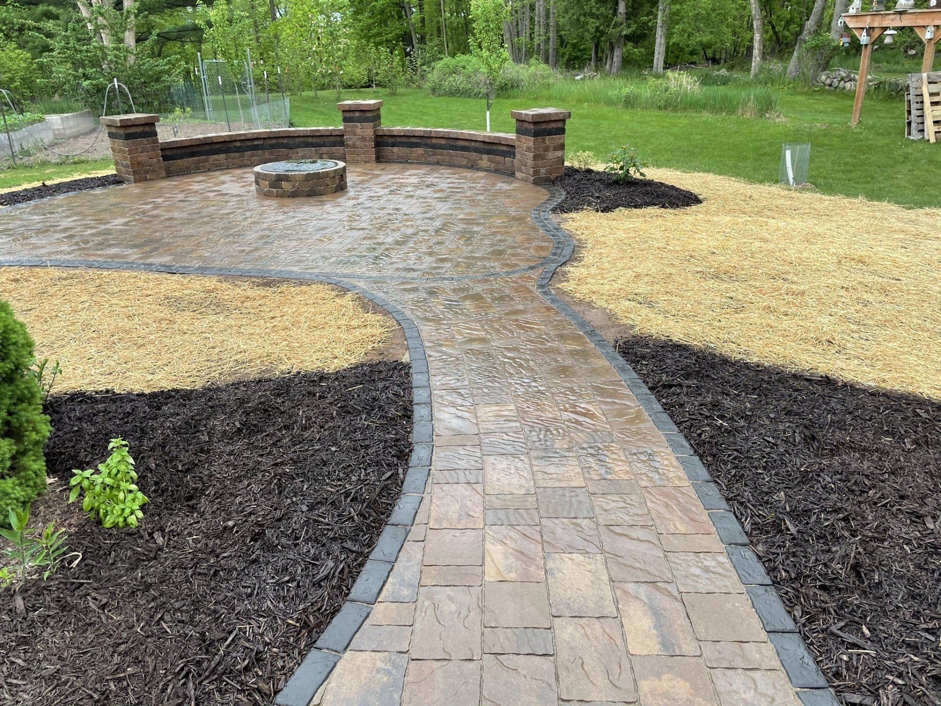 Brick patio with fire pit, bordered by brown and tan stone beds, path leading to it.
