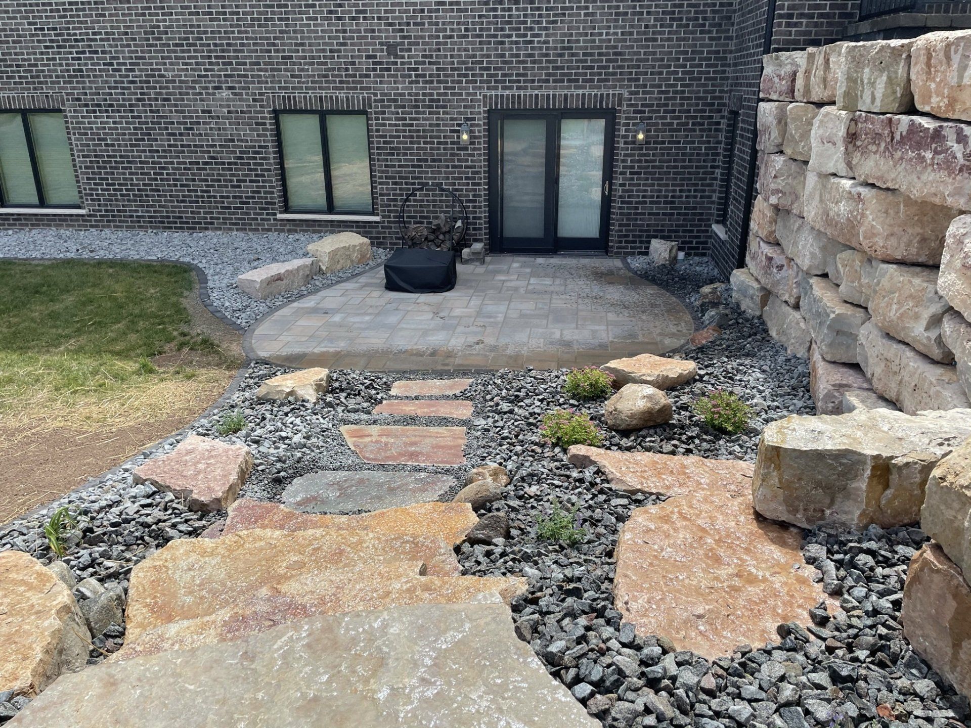 Stone pathway leading to a patio outside a brick building. Gravel and rock landscaping.