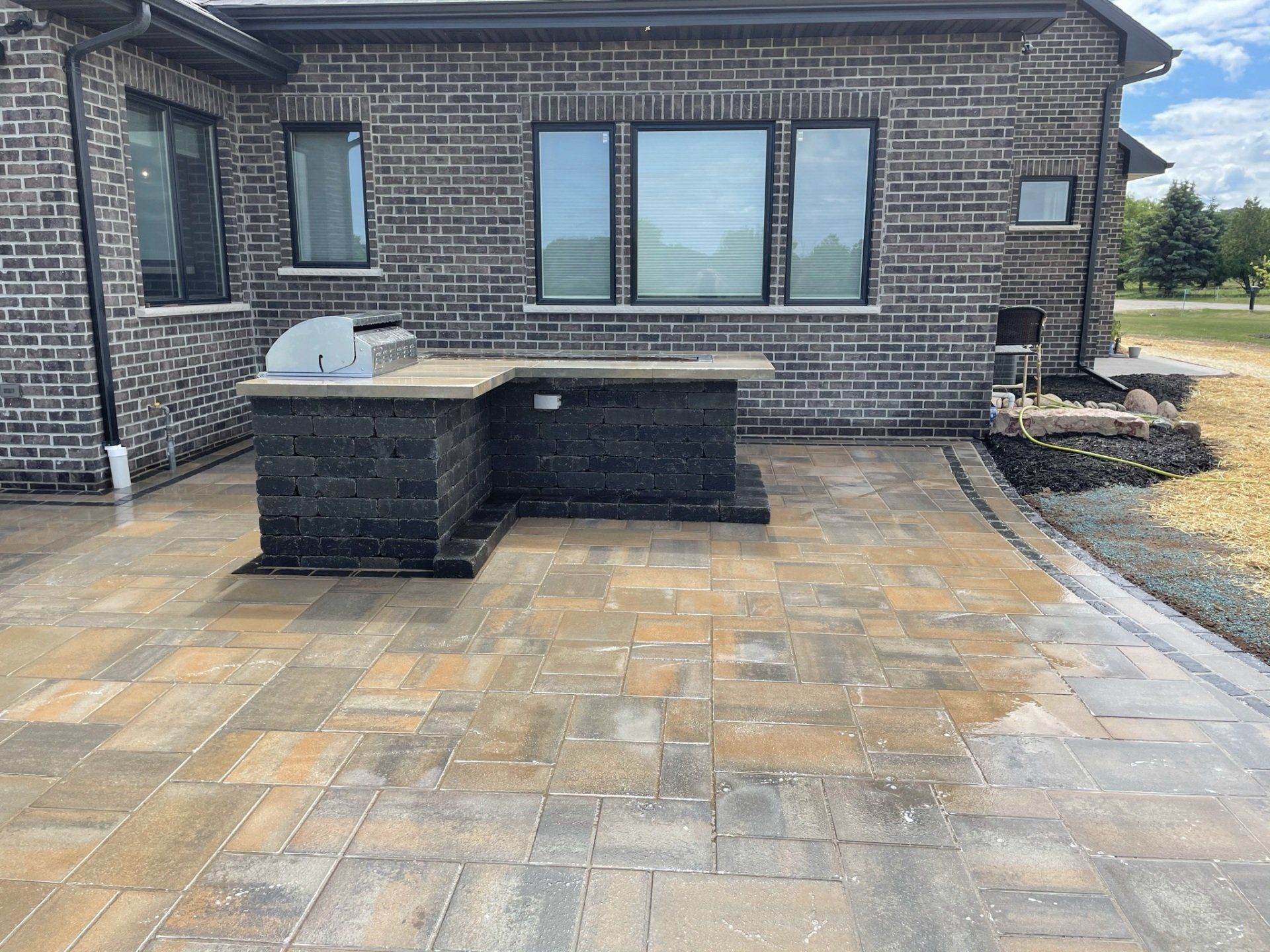 Brick home exterior with a paved patio and outdoor kitchen with a built-in grill.