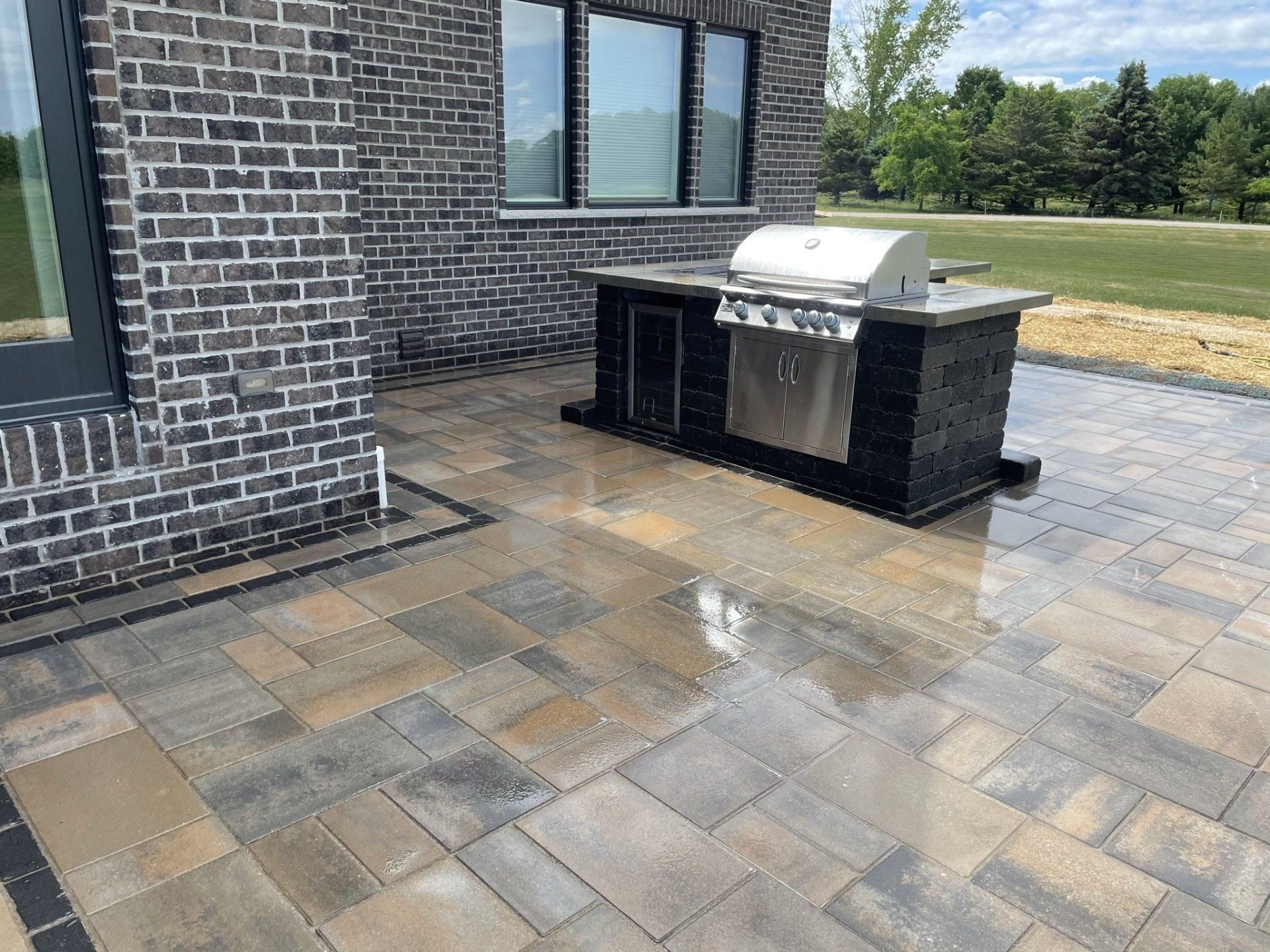 Patio with a grill built into a black stone island next to a brick building.
