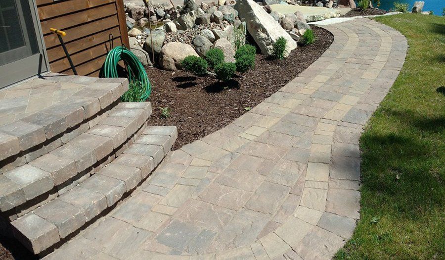 Stone pathway curves past steps and a landscaped border with rocks and plants.