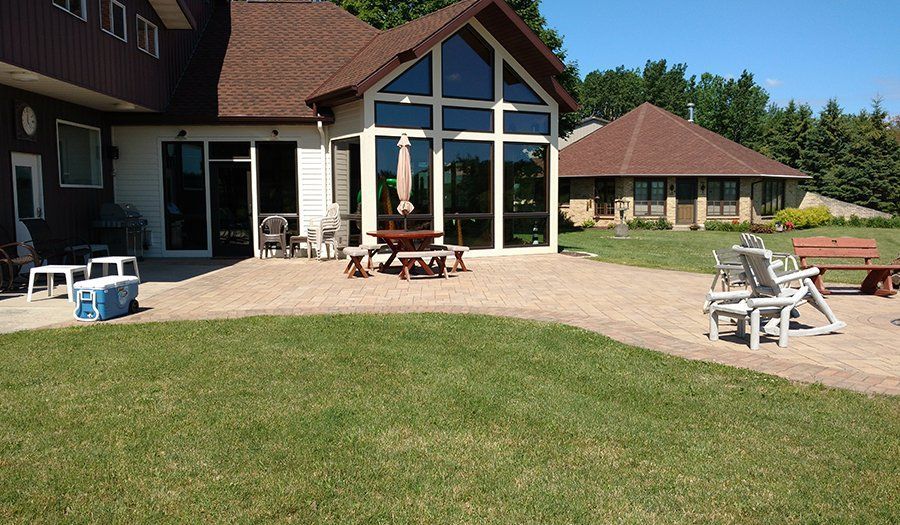 Backyard patio with lawn, picnic table, chairs, and two buildings.