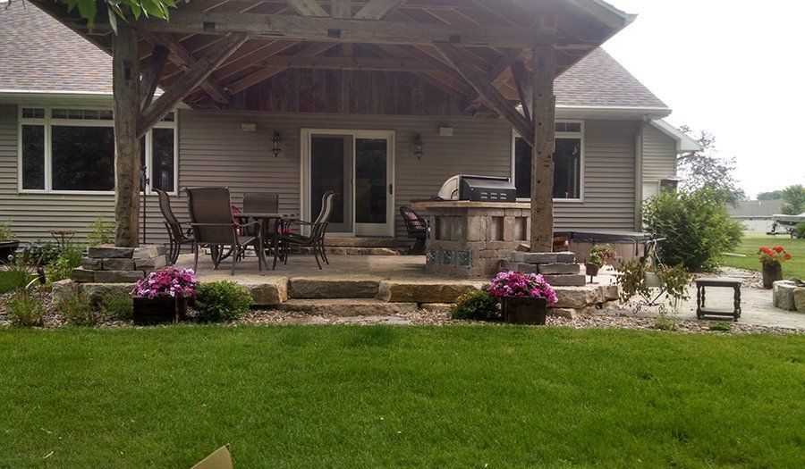 Backyard patio with wooden pergola, built-in grill, and flower beds.