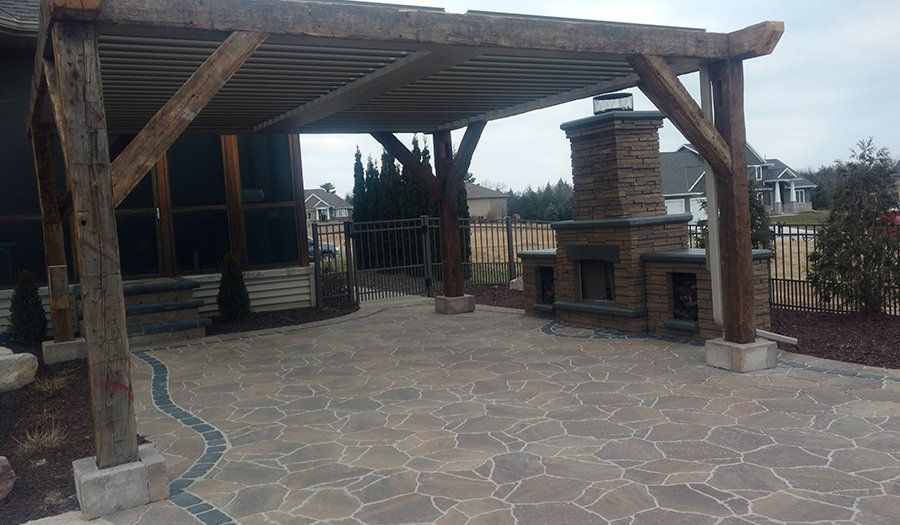 Wooden pergola over stone patio with outdoor fireplace.