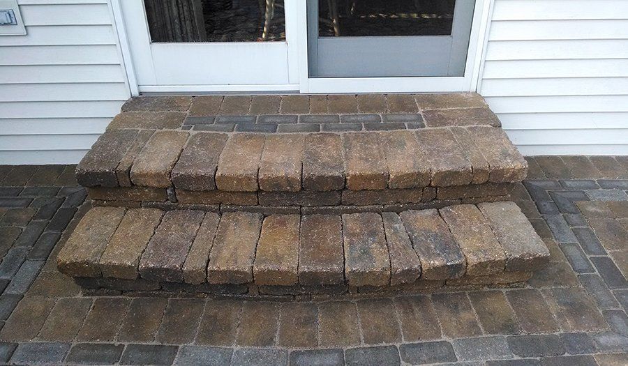 Brick steps leading to a white door, set against a background of light siding.