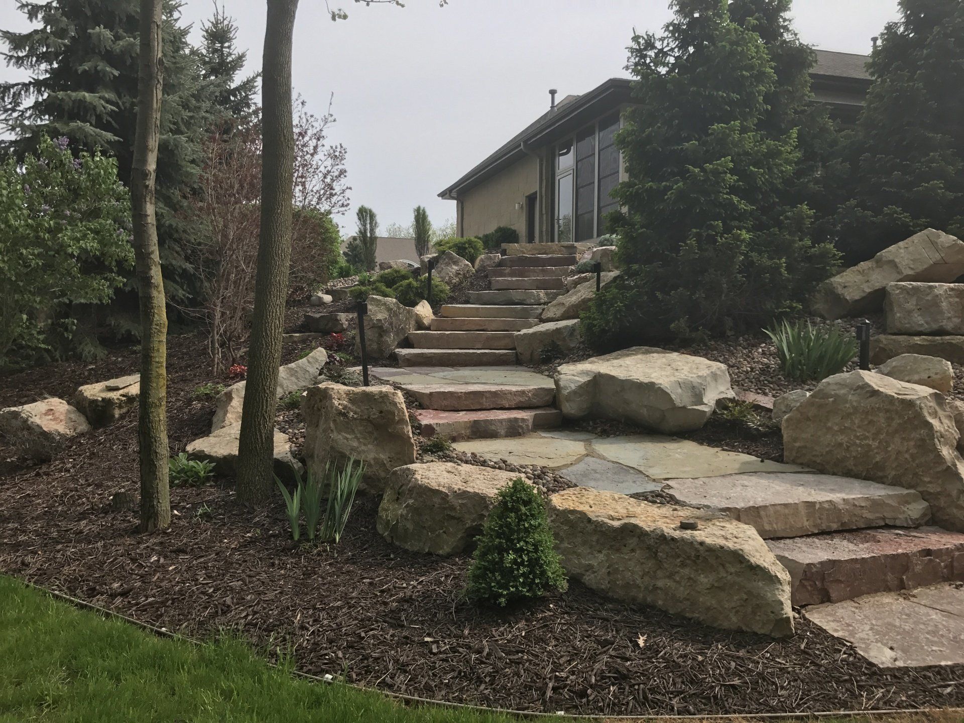 Stone steps lead up a landscaped hillside, with large rocks and greenery.