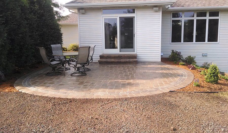 Outdoor patio with table and chairs next to a white house with a sliding door and windows.
