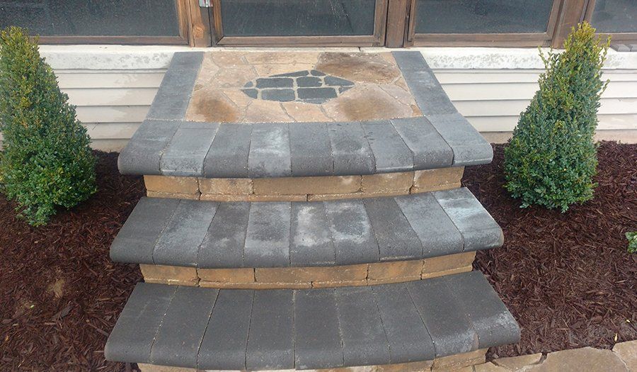 Brick steps leading to a door, flanked by green bushes in a mulch bed.