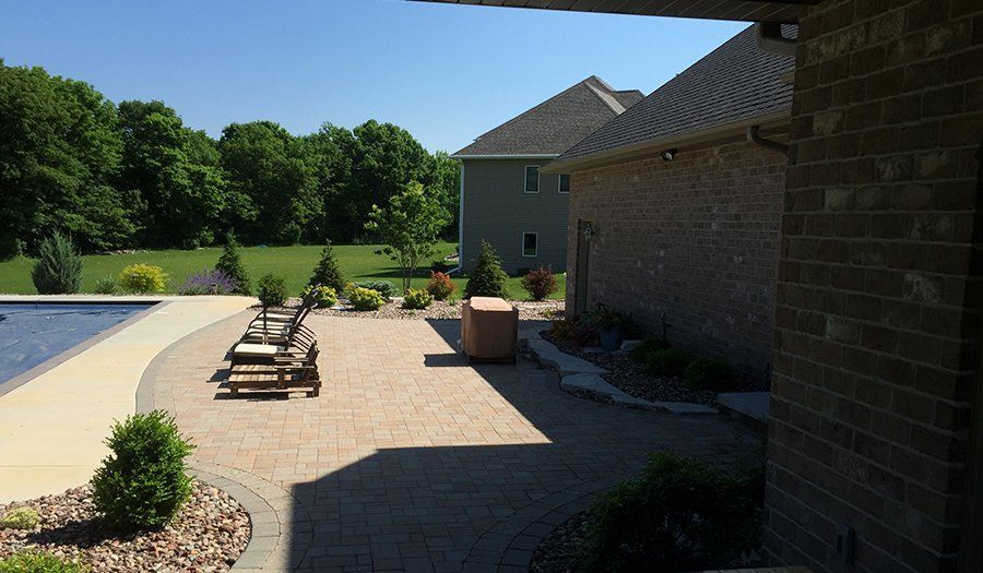 A sunny outdoor patio with a pool, lounge chairs, and a brick house.