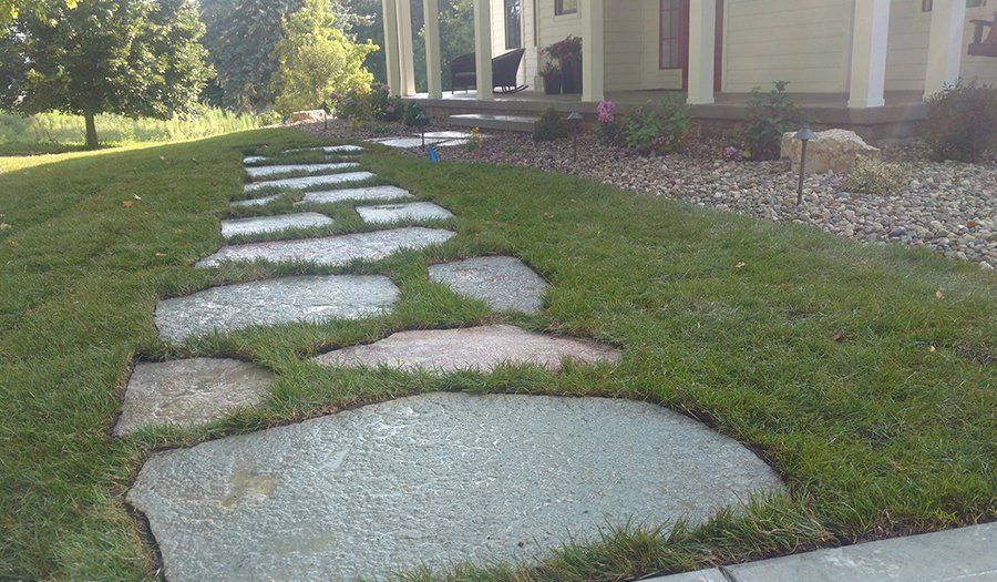 Stone pathway through a grassy yard leading to a house with a porch.