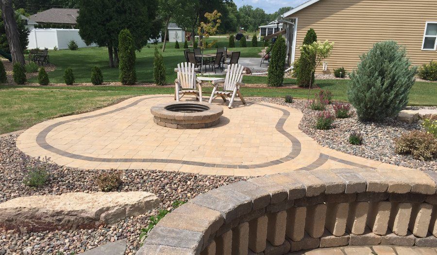Brick patio with fire pit, seating, and landscaping in a backyard.