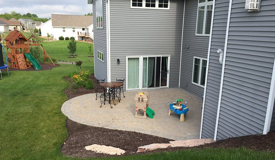 Backyard with a gray house, patio with toys, play set, and green lawn.
