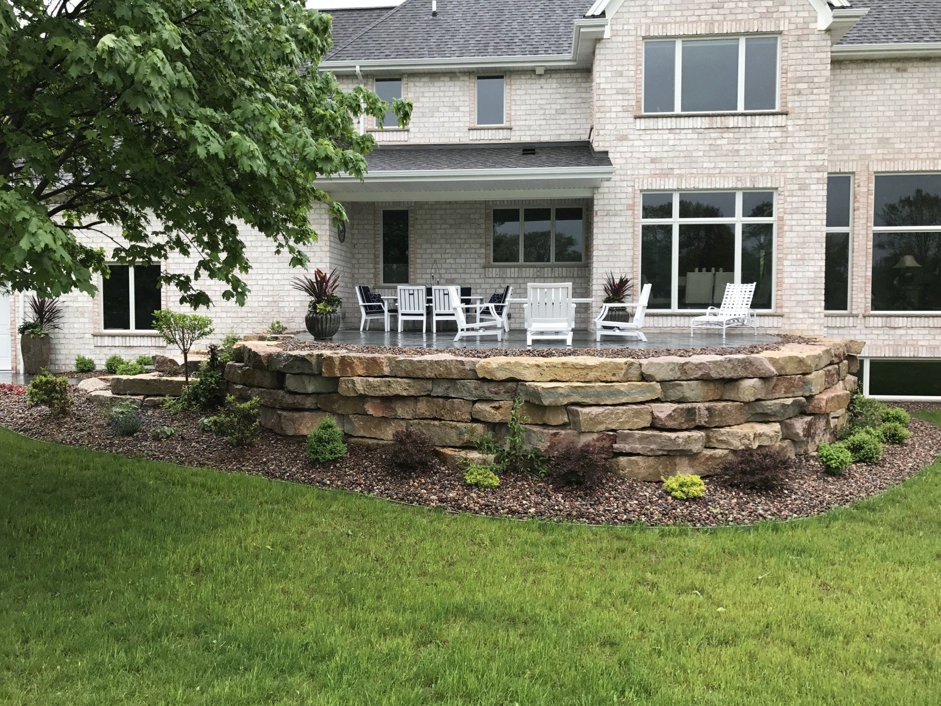 Backyard patio with stone retaining wall, seating, and a two-story brick house.