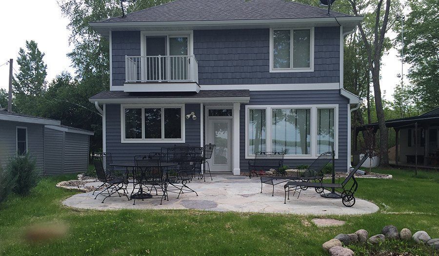 Two-story blue house with white trim and patio furniture on a concrete patio.