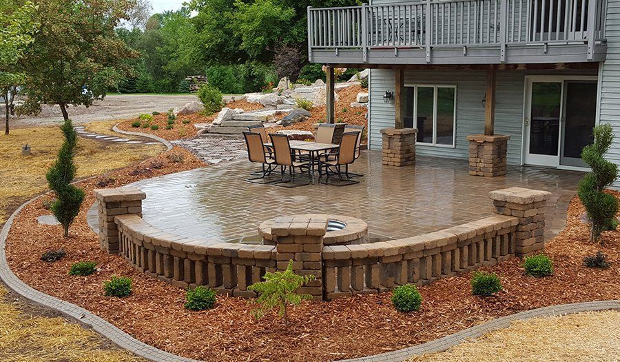 Patio with a fire pit, seating, and landscaping next to a house with a deck.
