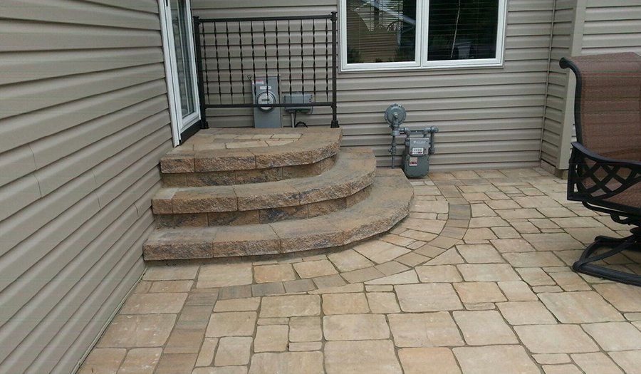 Stone steps lead to a door on a house with a brick patio and outdoor furniture.