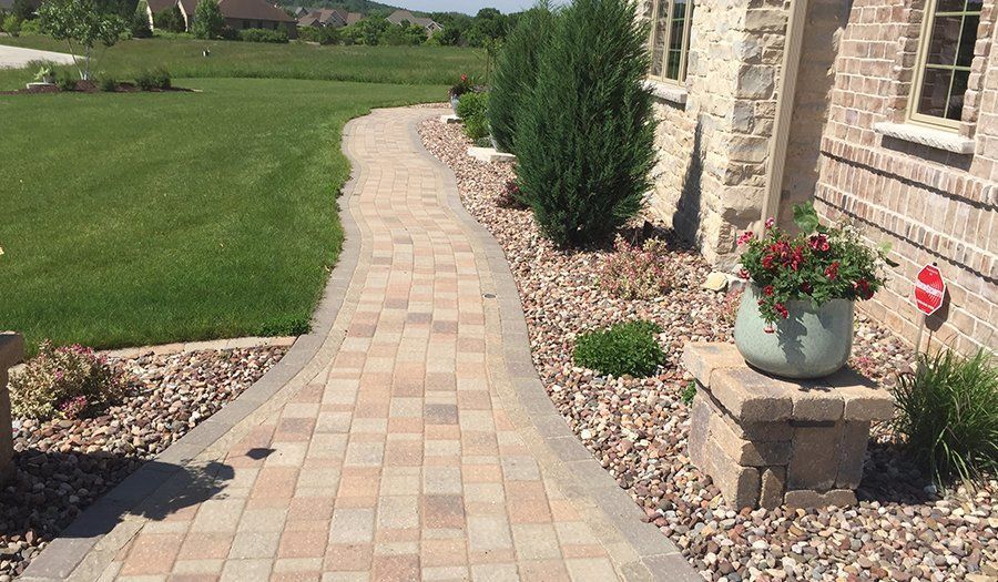 Brick pathway leads from lawn to house entrance, with shrubs and flower pot.