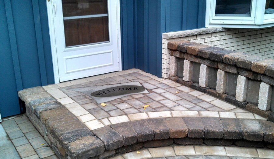Brick steps and landing with welcome mat in front of a blue house door.