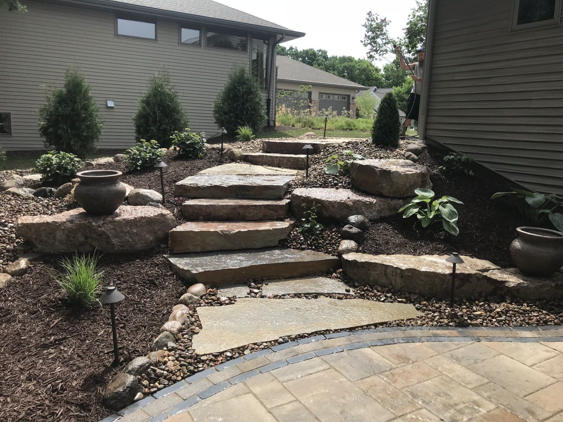 Stone steps ascend a landscaped garden with potted plants and pathway lights.