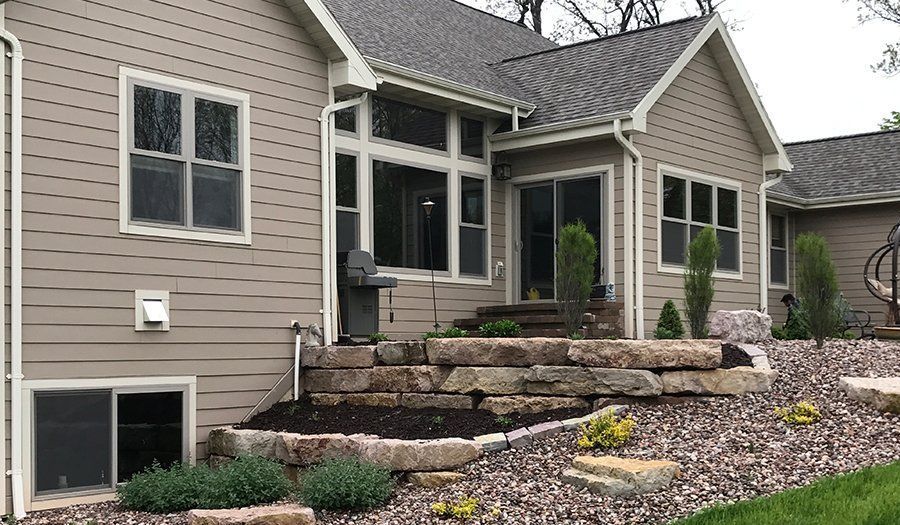 Tan house exterior with stone retaining wall, patio, and landscaping.