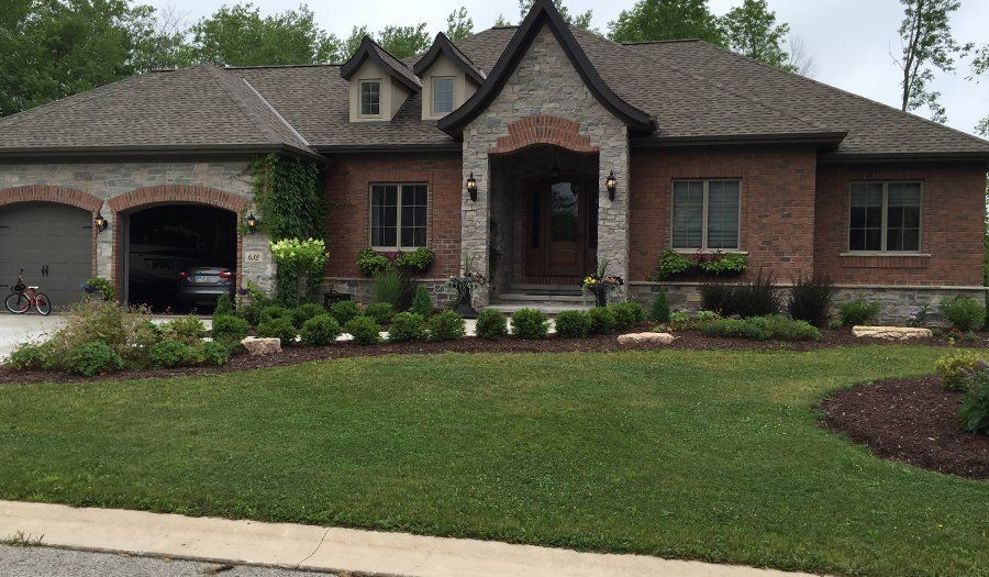 Brick and stone house with a garage, landscaping, and a well-manicured lawn on a cloudy day.