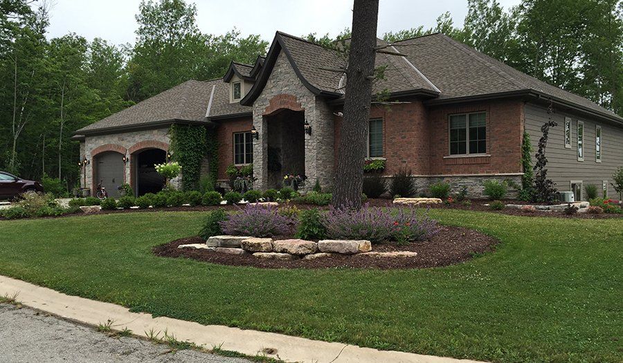 Stone and brick house with a well-manicured lawn and flower beds.