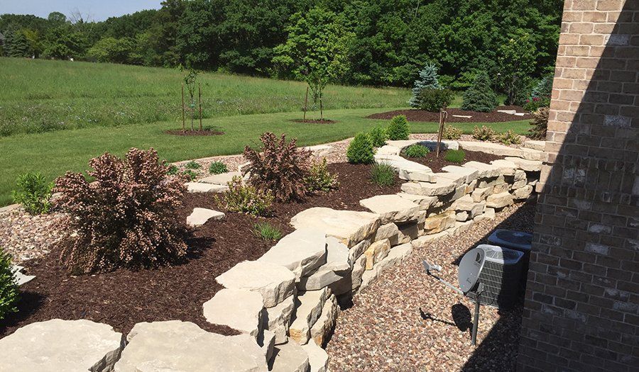 Stone retaining wall with a landscaped garden bed and a grassy field in the background.