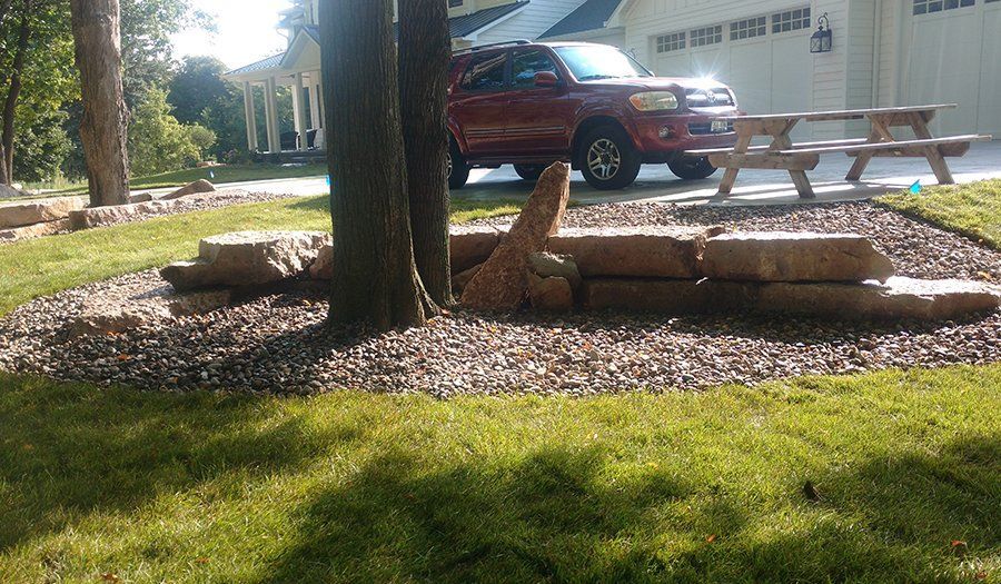 Landscaped tree with stone border and gravel bed. Red SUV parked nearby.