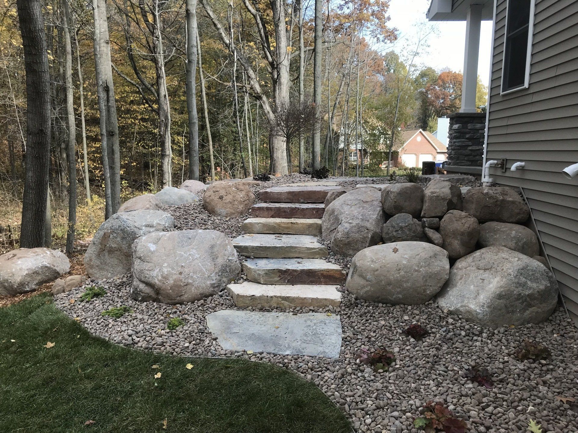 Stone steps lead up a hill, flanked by large boulders and gravel landscaping.