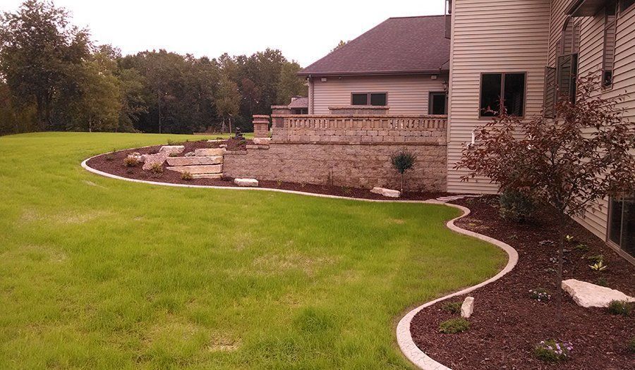 Green lawn with curved concrete border, stone retaining wall, and house.