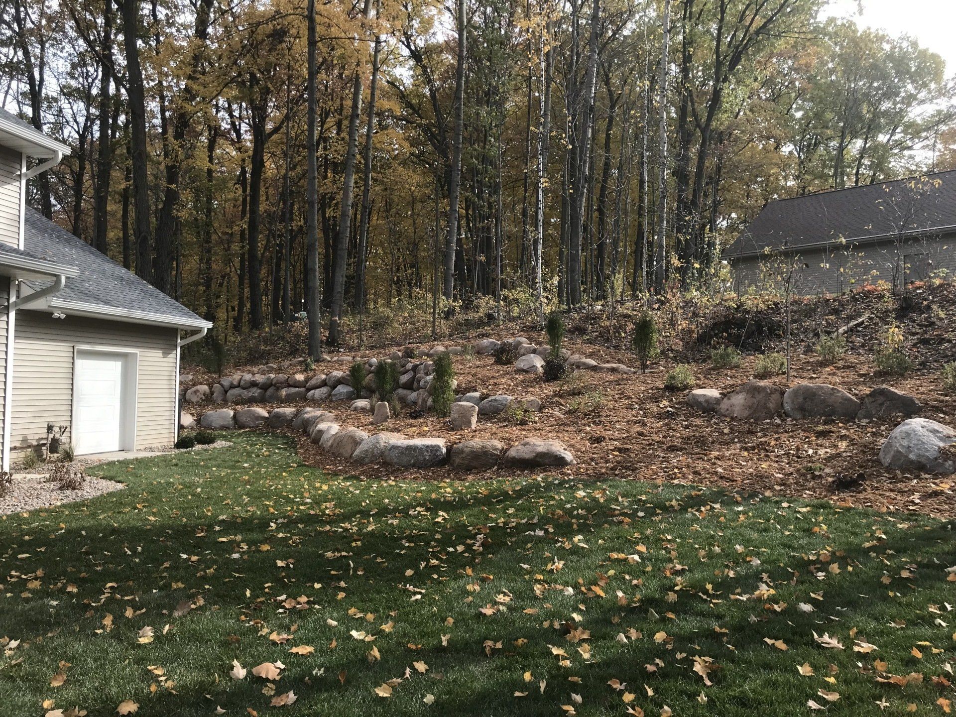 Backyard with lawn, rock walls, and trees in autumn.