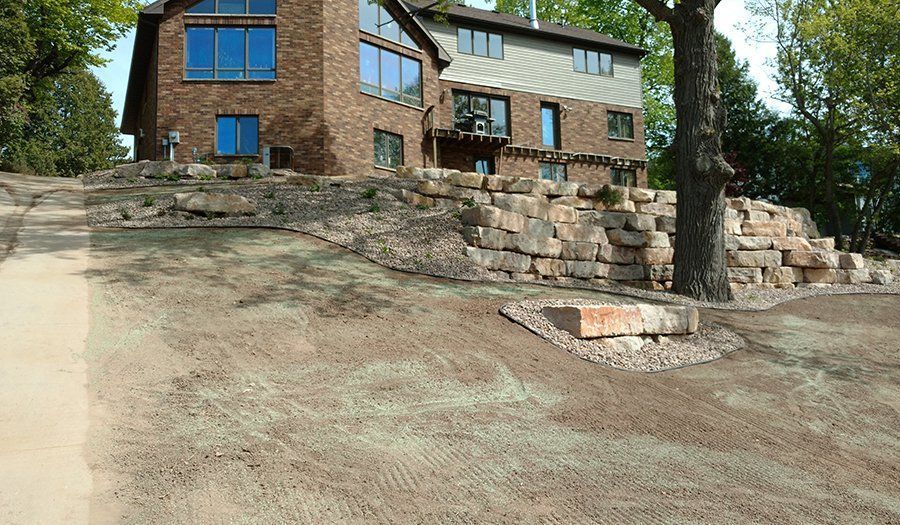Two-story brick and siding house with rock retaining wall and freshly seeded, sloped lawn.