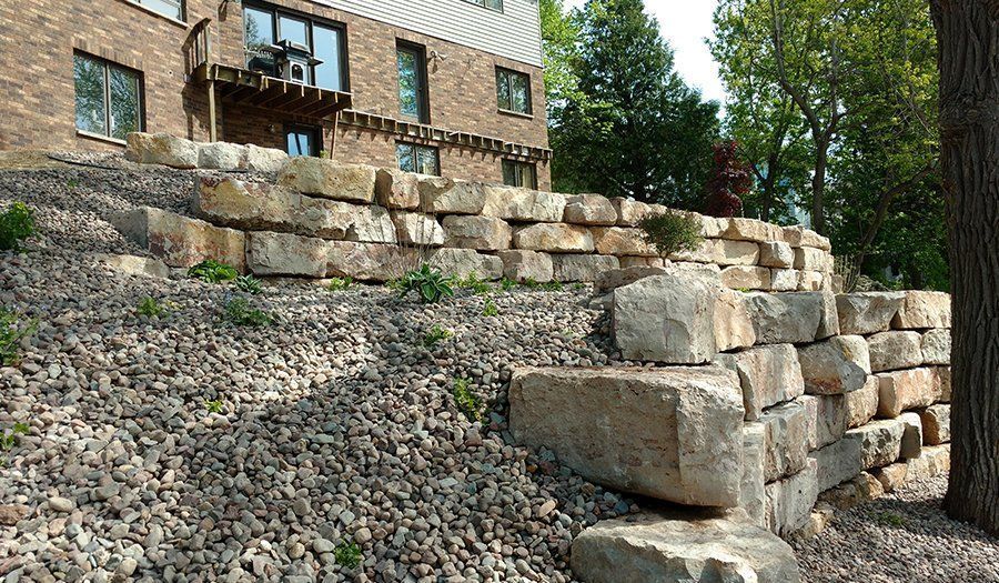 Stone retaining wall with a house in the background and a tree on the right.