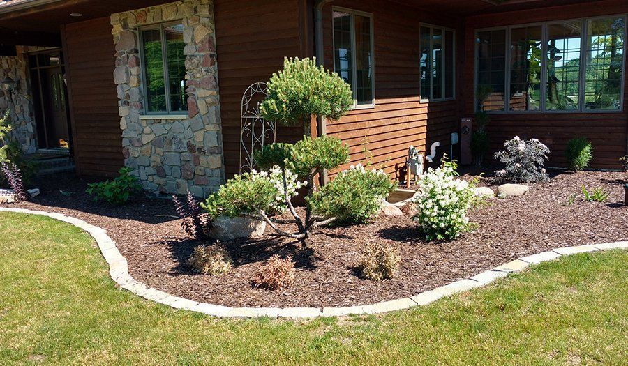 Brown house exterior with landscaped bed, curved edging, and green lawn.