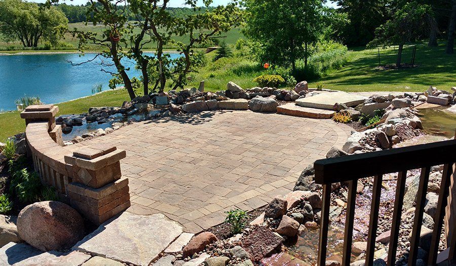 Patio with brick pavers overlooking a lake. Stone retaining walls and landscaping surround the patio.